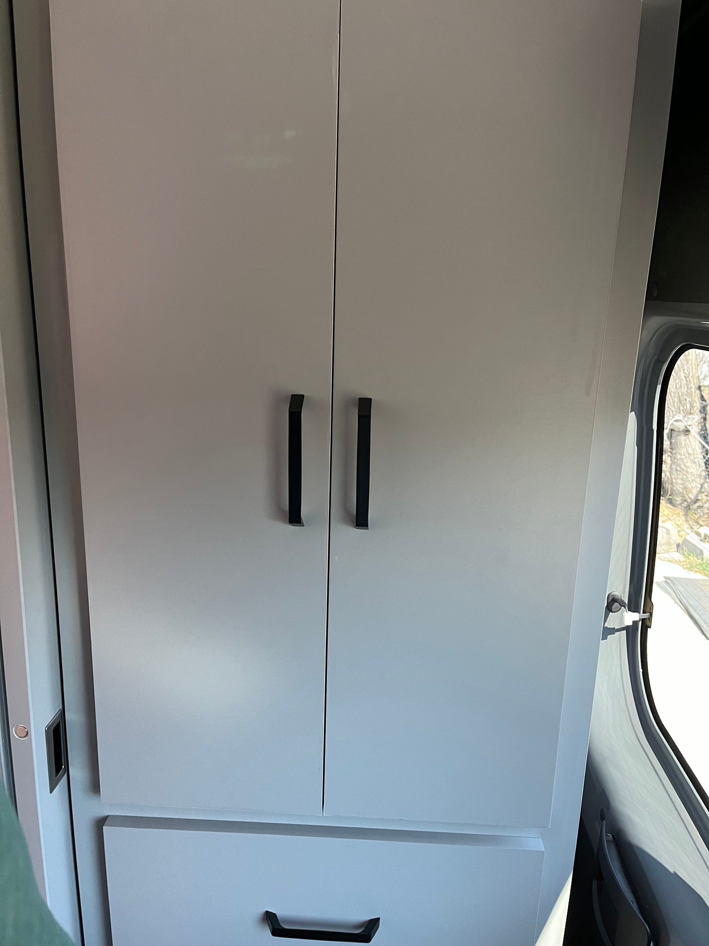 Sleek light gray cabinets with black bar handles and a bottom drawer, essential storage in an RV rental interior, with a window view.