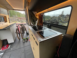Cozy RV rental interior with kitchen, bikes, and scenic volcanic rock and forest views. Ready for adventure!