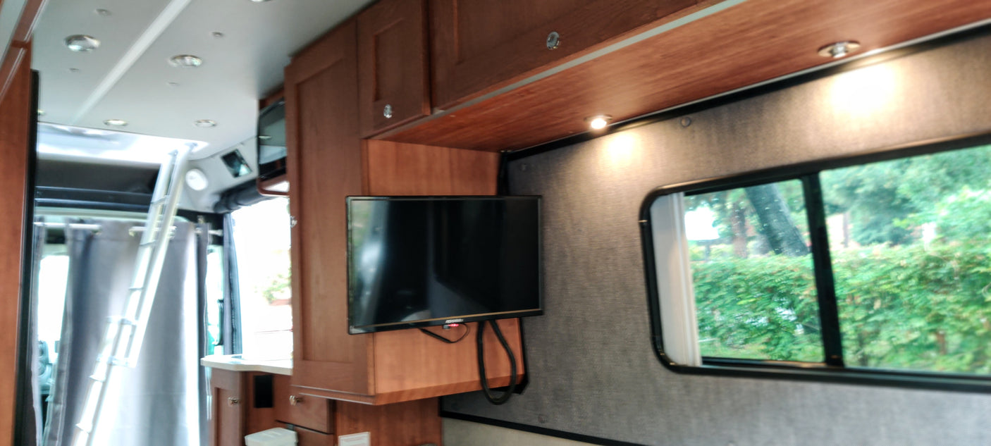 RV rental interior: wooden cabinets, wall-mounted TV, and a ladder to an upper bunk, with a scenic window view.
