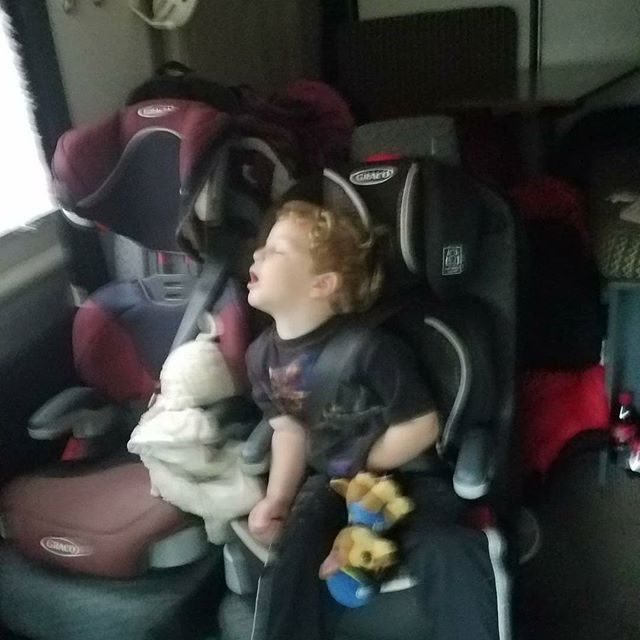 A young child, eyes closed, sleeps peacefully in a car seat inside an RV rental. Perfect for cozy family travel.