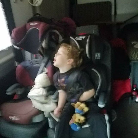 A young child, eyes closed, sleeps peacefully in a car seat inside an RV rental. Perfect for cozy family travel.