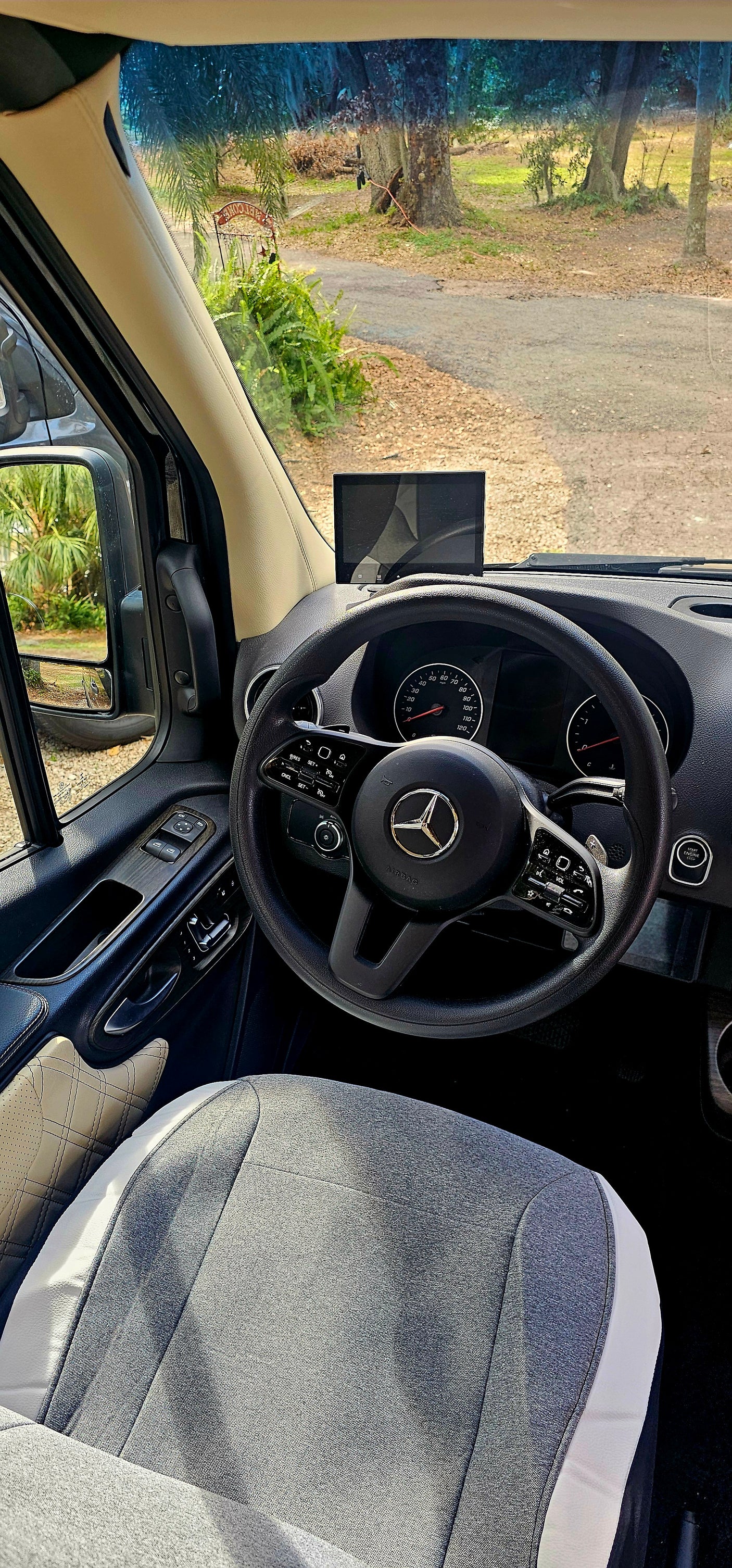 Interior view of a modern Mercedes-Benz rv rental, showing the dashboard, steering wheel, and front window scene.