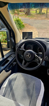 Interior view of a modern Mercedes-Benz rv rental, showing the dashboard, steering wheel, and front window scene.