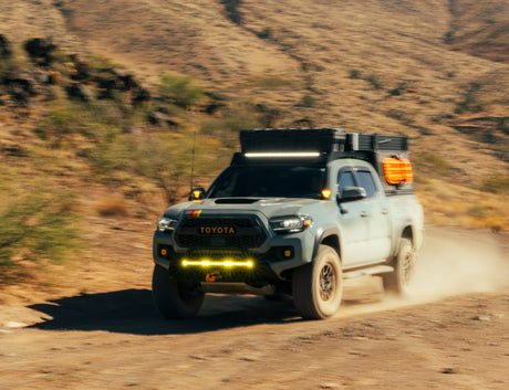A modified Toyota Tacoma overlanding truck, ideal for an off-road RV rental adventure, kicks up dust in a desert landscape.