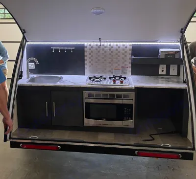 This RV rental boasts a compact outdoor kitchen: sink, two-burner stove, microwave, and storage. Perfect for adventurers.
