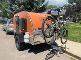 Orange teardrop RV rental with mountain bikes for outdoor adventures. Perfect for camping trips.