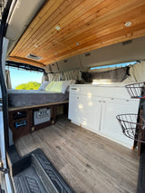Modern RV rental interior featuring a comfy bed, kitchen, wood ceiling, and scenic window views.