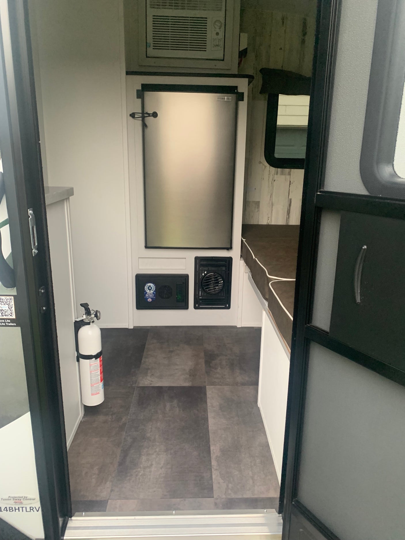 Compact RV rental interior with refrigerator, AC, and a fire extinguisher. Ideal for comfortable travel.