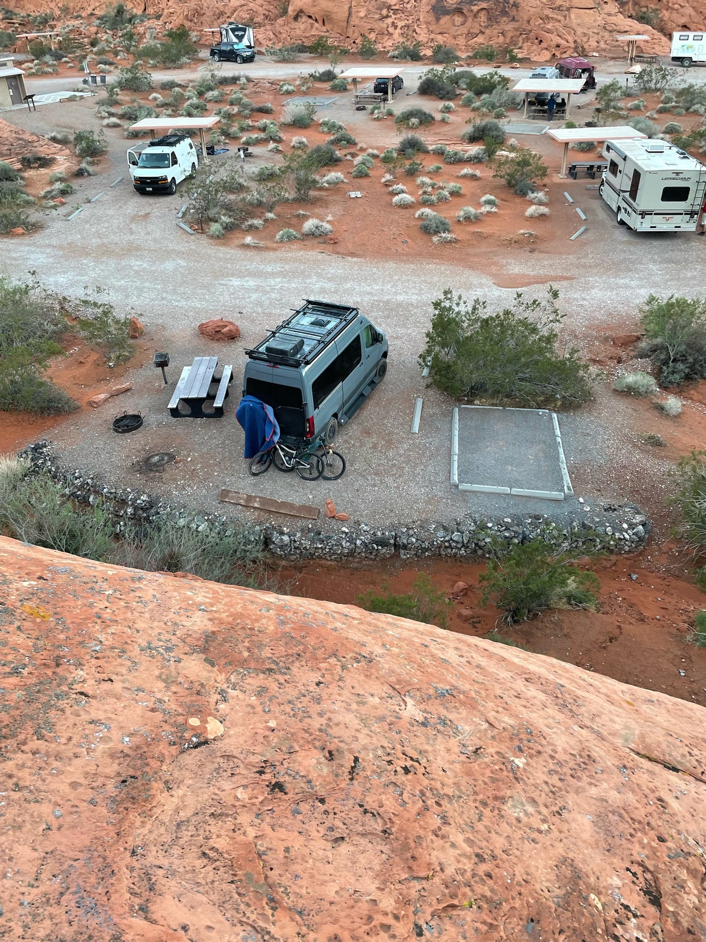 High-angle view of a desert RV campsite with several RVs and vans, like an rv rental, nestled among red rocks.