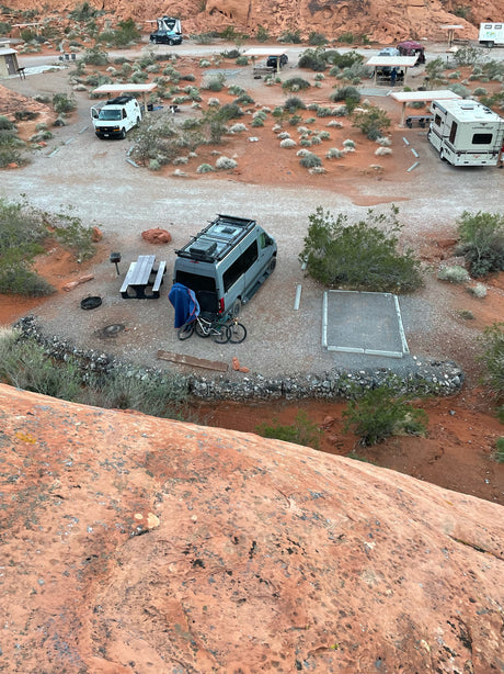 High-angle view of a desert RV campsite with several RVs and vans, like an rv rental, nestled among red rocks.