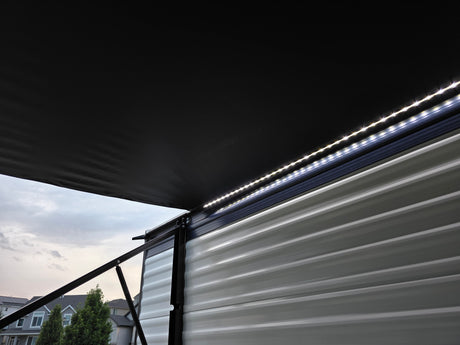 This close-up of an RV rental shows a black extended awning with bright LED strip lights illuminating the ribbed side paneling.