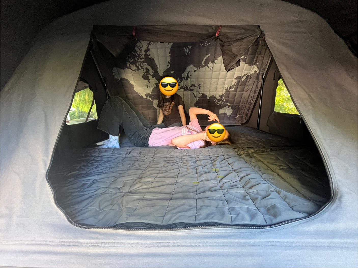 Inside a spacious RV rental: two people relaxing on a quilted bed with a cool world map wall. Enjoying a comfy road trip!