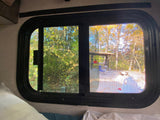 View from an RV rental window showing a colorful autumn campsite with trees, a picnic shelter, and outdoor chairs.