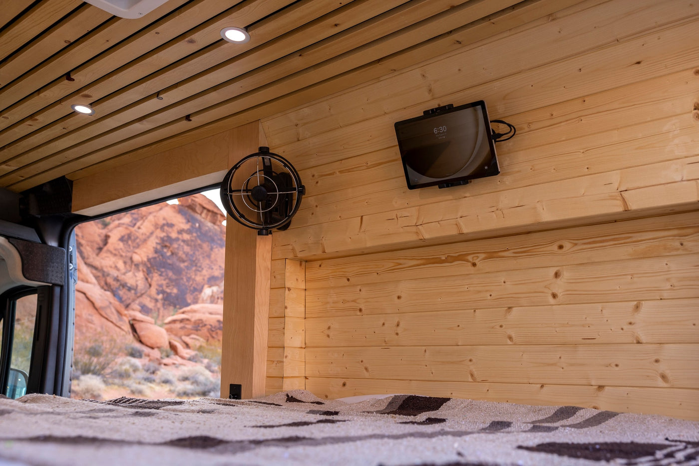Cozy rv rental interior with wood walls, ceiling lights, fan, tablet, and a scenic desert view from the bed. — photo 6