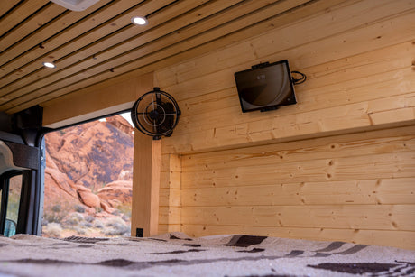 Cozy rv rental interior with wood walls, ceiling lights, fan, tablet, and a scenic desert view from the bed.