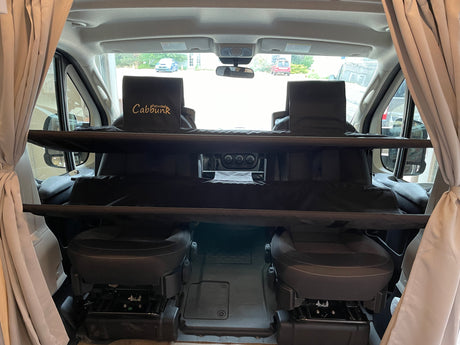 Interior of an RV rental showing a Cabbunk system installed over the driver and passenger seats for added sleeping.