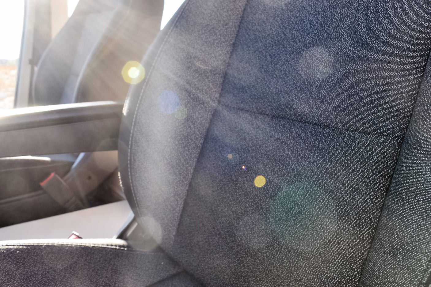 Inside an RV rental: a sunlit passenger seat, highlighting its textured fabric and armrest. Ready for adventure!