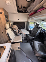 View inside an RV rental showing the living area with swivel seats, a child car seat, dining table, and kitchen counter.