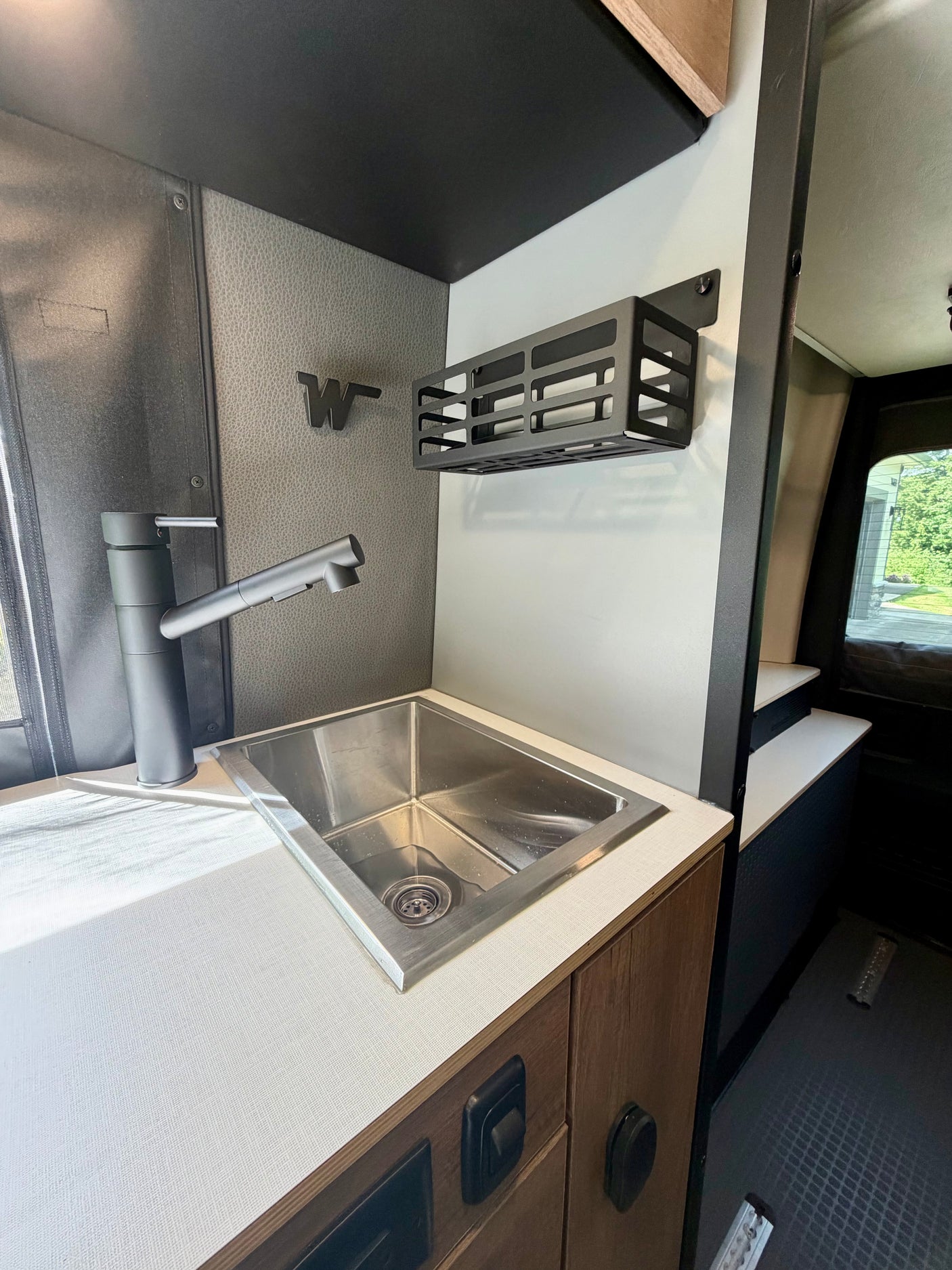 Compact RV rental kitchen features stainless steel sink, matte black faucet, white counter, and wall-mounted storage.
