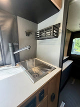 Compact RV rental kitchen features stainless steel sink, matte black faucet, white counter, and wall-mounted storage.