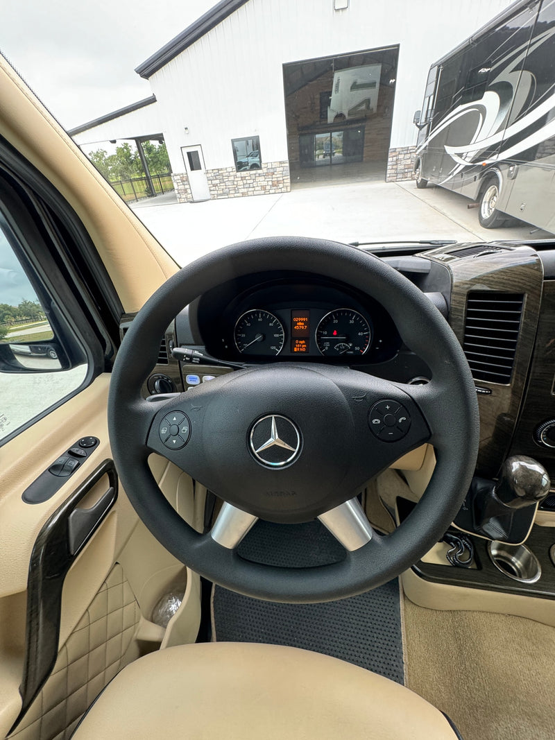 Driver's view in an RV rental, showing Mercedes steering wheel, dash, and a large RV outside a modern building. — photo 13