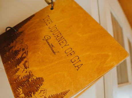 Wooden guestbook, "THE JOURNEY OF GIA" title, engraved mountains. Ideal for an RV rental adventure.