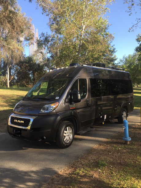 Get ready for your next adventure with this dark grey Ram ProMaster RV rental, parked at a sunny campsite.