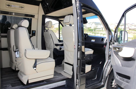 This luxury RV rental's interior boasts cream captain's chairs and wood-look flooring, with open doors showing the driver's area.