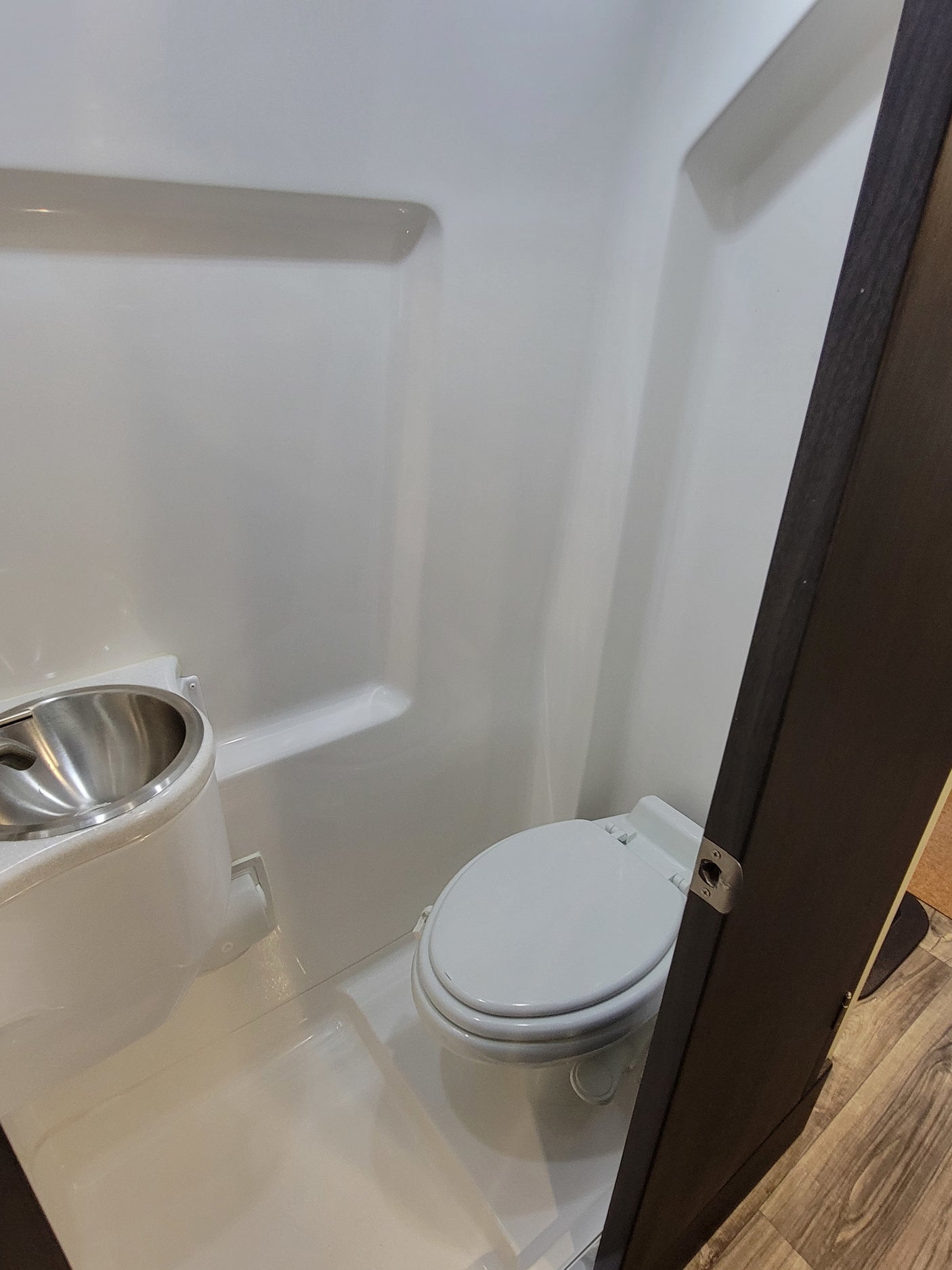 A small, white RV rental bathroom equipped with a toilet and a compact stainless steel sink.