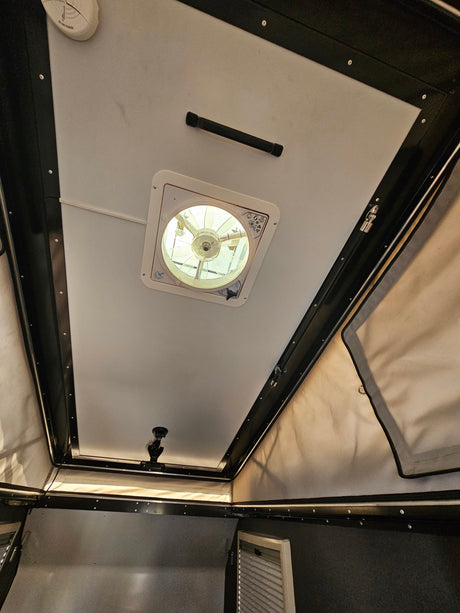 Inside an RV rental: Looking up at the pop-top camper ceiling with a vent fan, grab handle, and smoke detector.