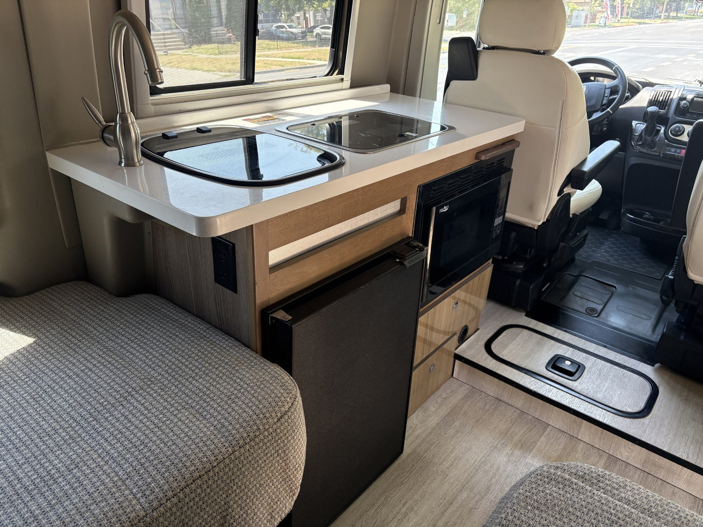 RV rental interior: A compact kitchenette with sink, cooktop, microwave, and fridge, visible next to the driver's seat. — photo 6