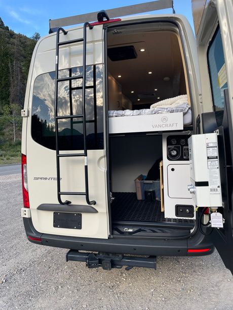 RV rental Sprinter camper van's rear view, with open doors showcasing its VANCRAFT interior, cozy bed, and water system.