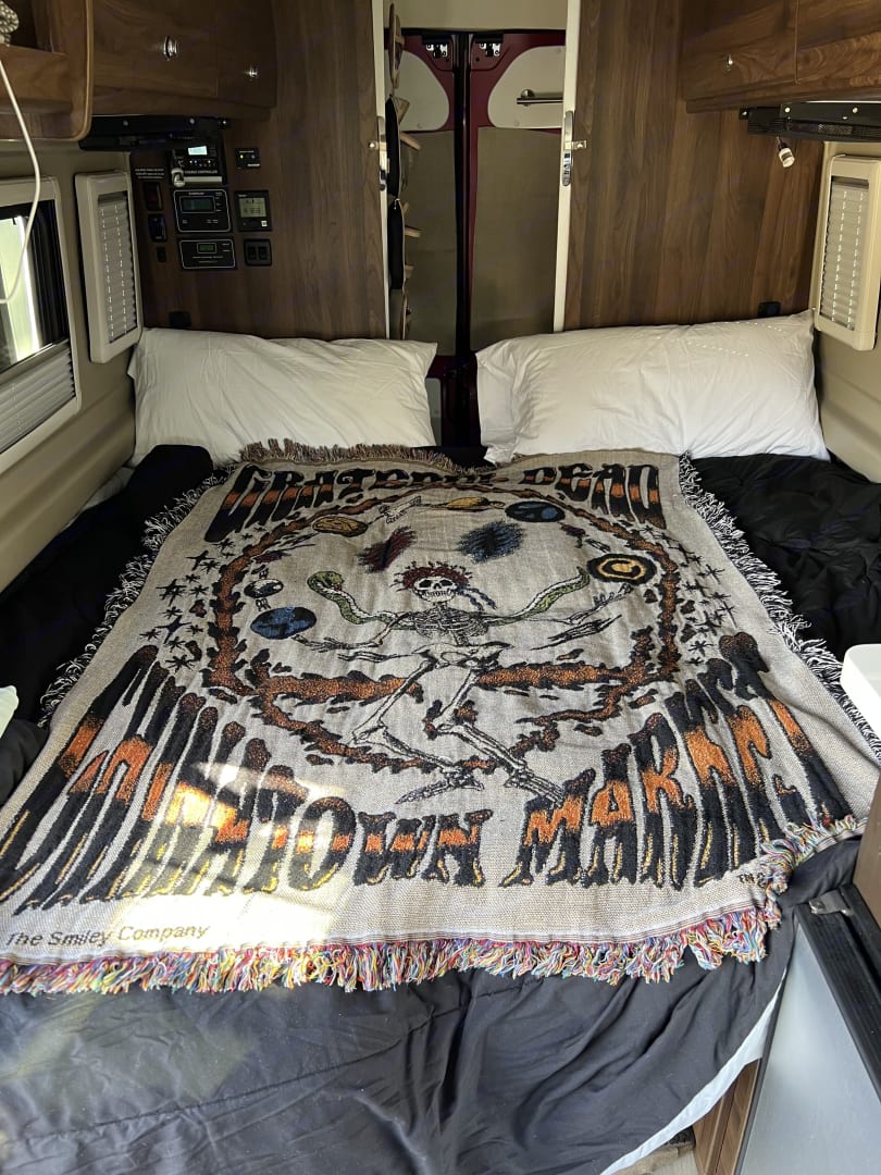  and bed with checkered rug in the main living space.|Two red RV rental vans with solar panels create a cozy outdoor gathering space on wood chips for friends.|This RV rental's compact kitchen boasts a sink — photo 8