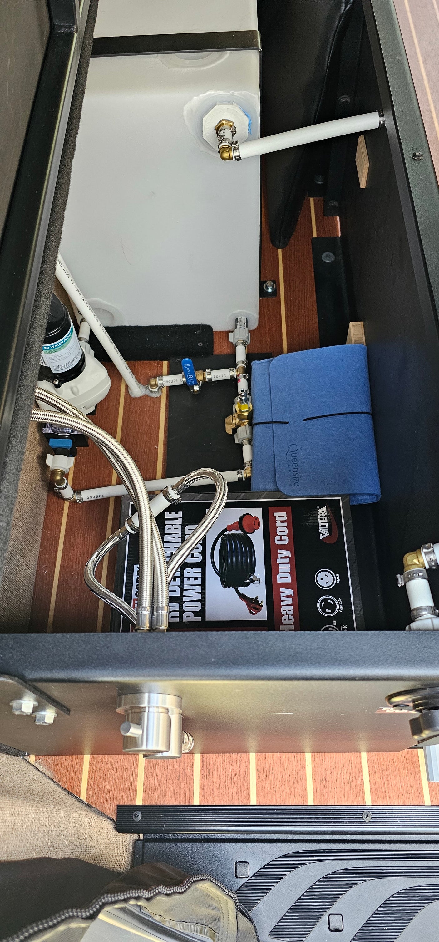 RV rental interior: a compact water system featuring a white tank, pump, plumbing, and power cord for reliable travel.