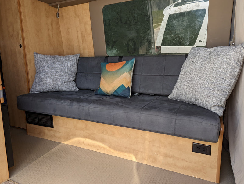 Cozy RV rental interior: a grey bench with pillows, window, and power outlets. Essential features for your travel comfort. — photo 3