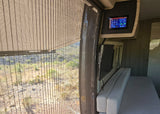 Inside this RV rental: a large window with desert landscape, overhead control panel, TV, and bench seating.