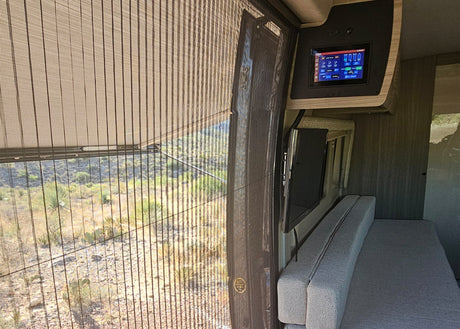 Inside this RV rental: a large window with desert landscape, overhead control panel, TV, and bench seating.