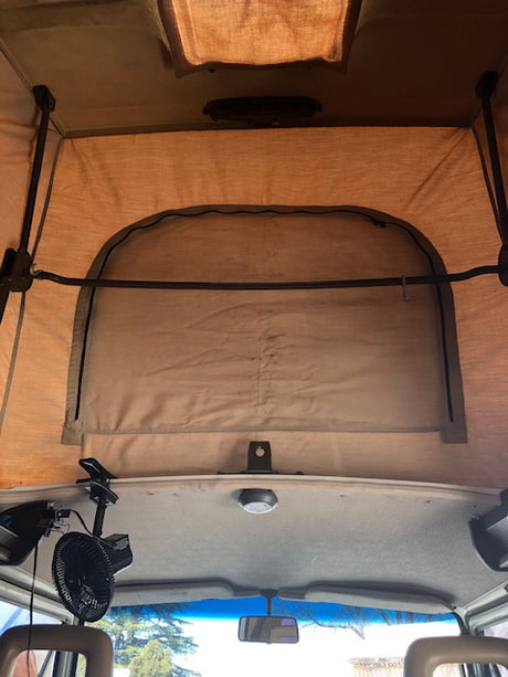 View inside an RV rental: Pop-top camper bed area stretches to the front cabin and windshield, featuring a fan.