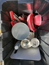 RV rental kitchen kit: A black bin filled with red utensils, pink bowls, metal pots, cutting board, and drinkware.