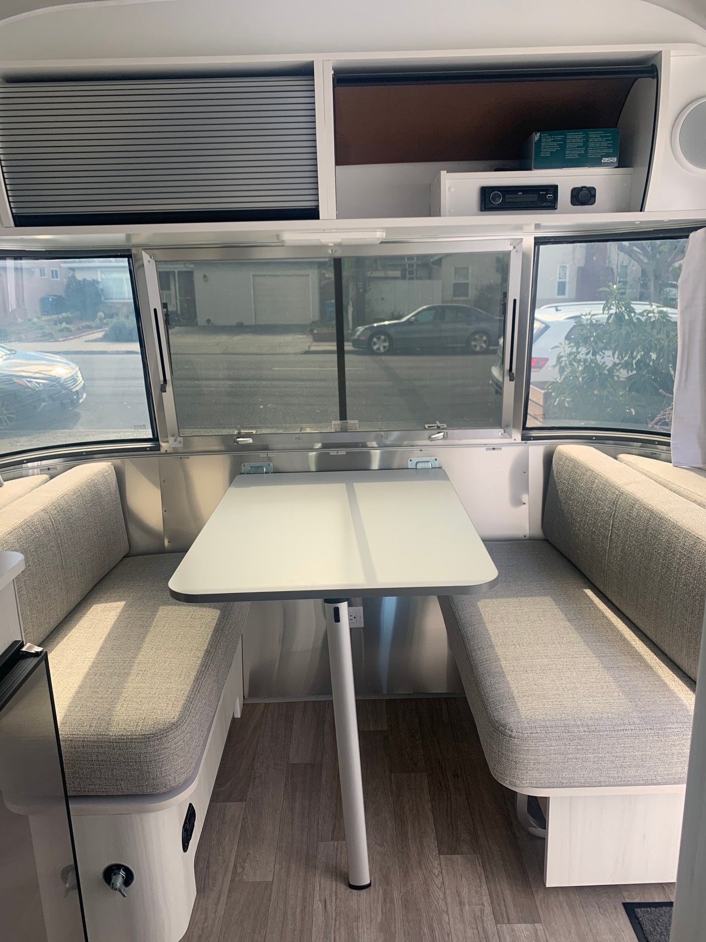 Bright, modern RV rental dinette with gray upholstered benches & table. Panoramic windows show street views. — photo 13
