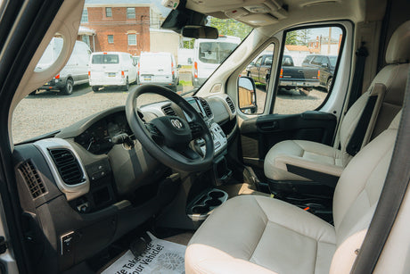 View of an RV rental van's interior: driver's seat, dashboard, and steering wheel. Other vans are visible outside.