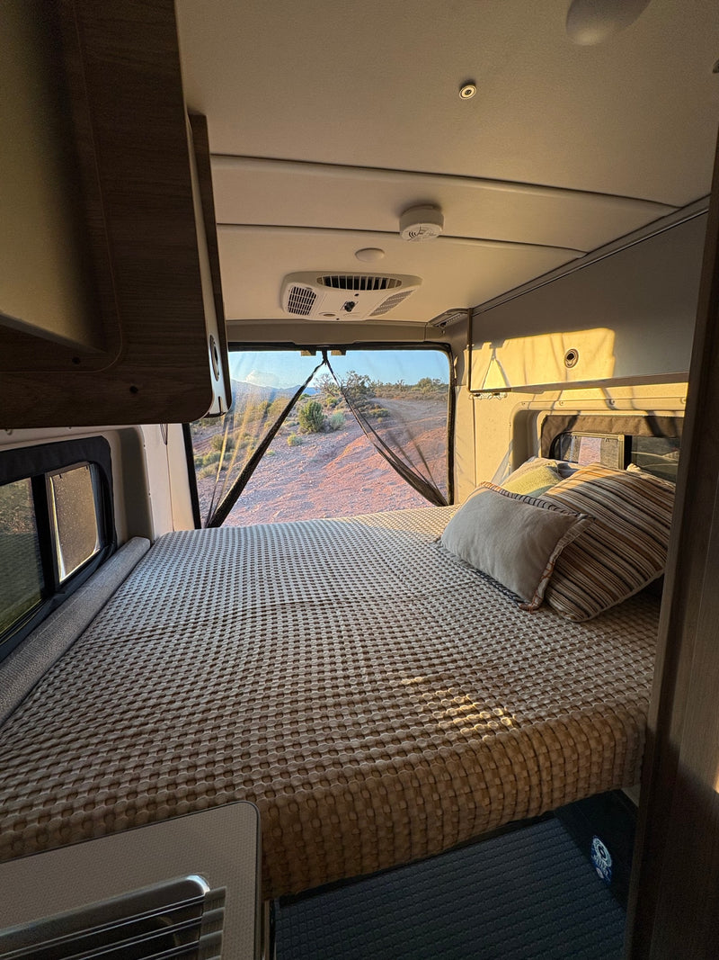 Inside this RV rental, a comfy bed faces a large, screened window with a sunlit desert view. Perfect for camping trips. — photo 10