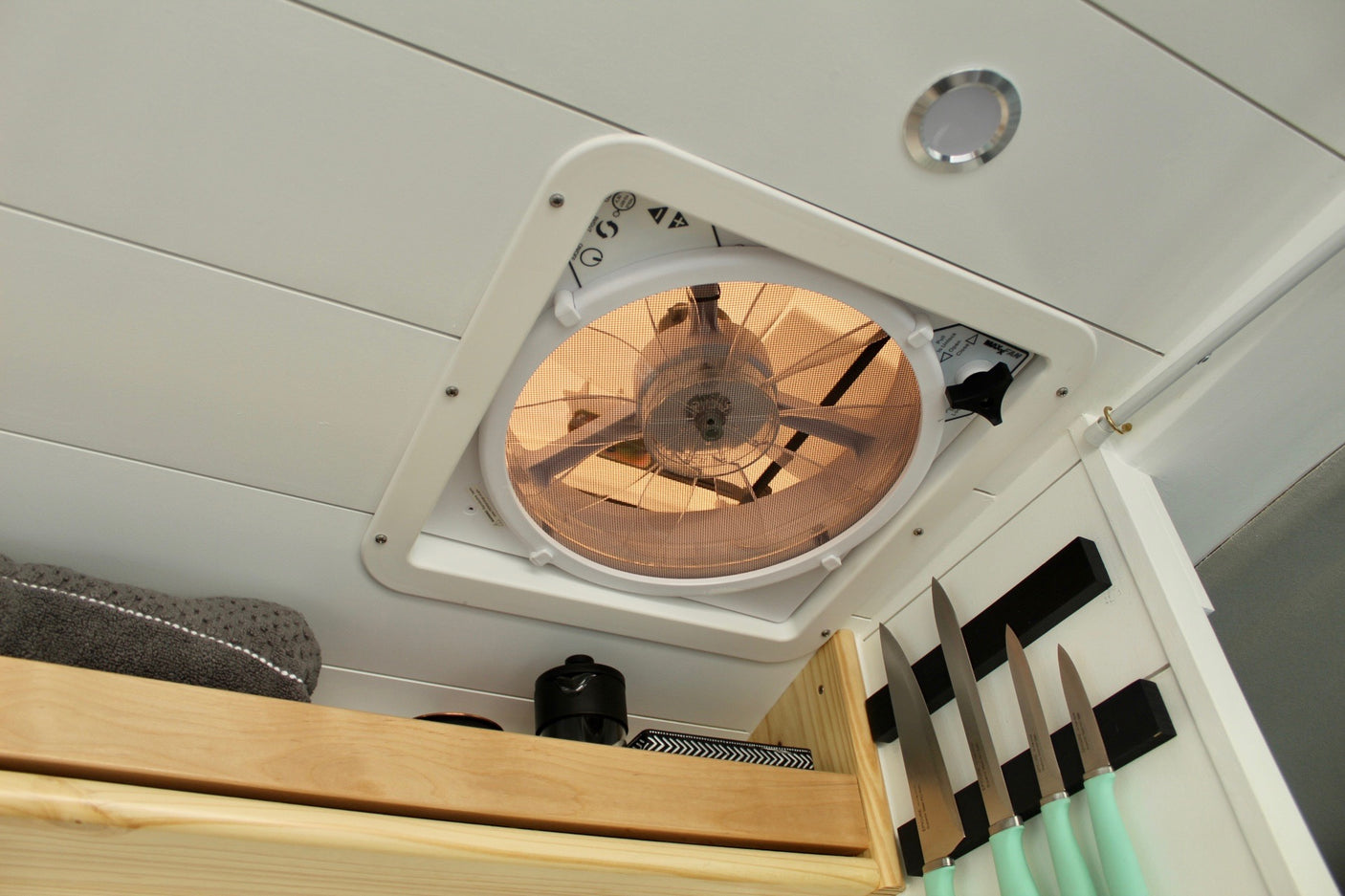 RV rental's functional ceiling: MaxxAir fan, LED light, & magnetic knife storage. Compact van kitchen design.