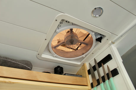 RV rental's functional ceiling: MaxxAir fan, LED light, & magnetic knife storage. Compact van kitchen design.