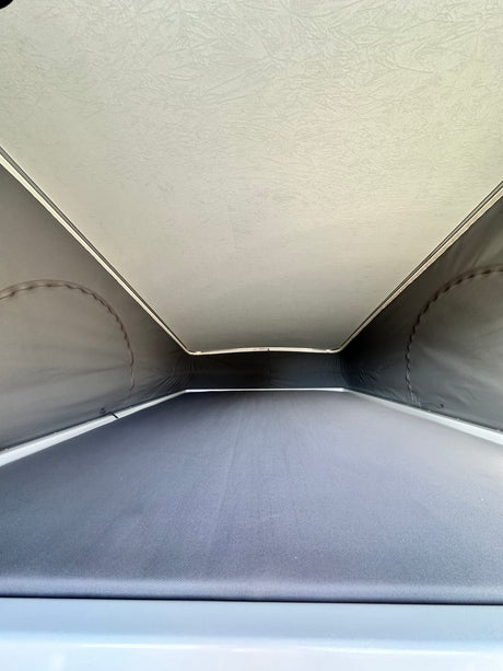 RV rental pop-top camper's interior: View of the light-colored elevated sleeping area and dark fabric walls.