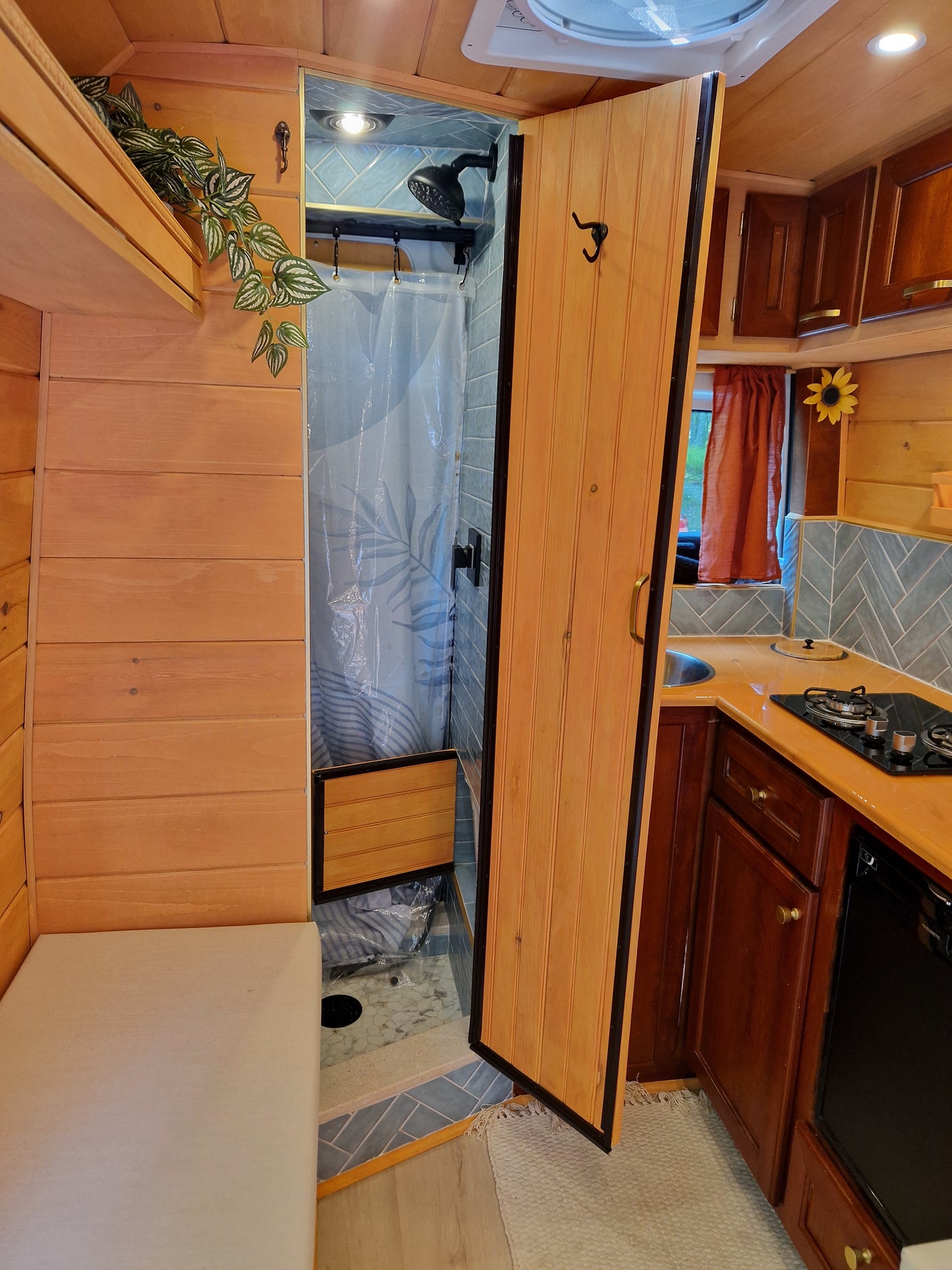 Inside an RV rental: Compact kitchen with stovetop & sink, plus a clever, tiled shower hidden behind a wooden door.