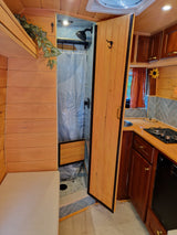 Inside an RV rental: Compact kitchen with stovetop & sink, plus a clever, tiled shower hidden behind a wooden door.