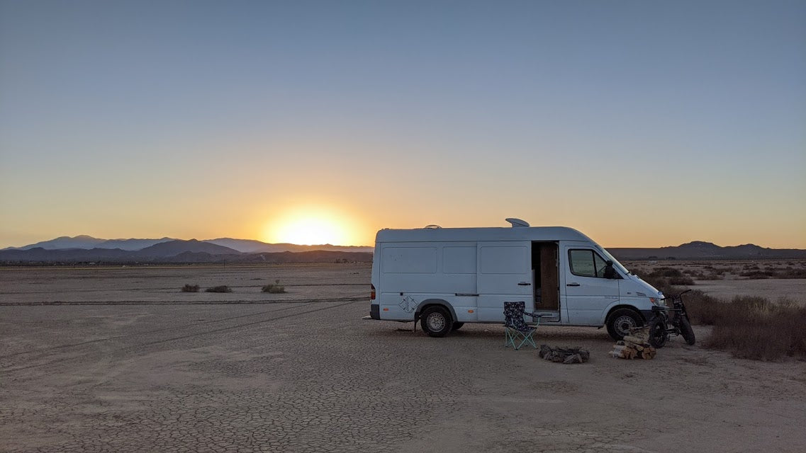 An RV rental camper van at sunset in a vast desert with distant mountains. Perfect for off-grid camping and adventure.