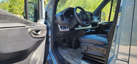 Open door reveals the spacious interior of a modern RV rental van: driver's seat, dashboard, and steering wheel.