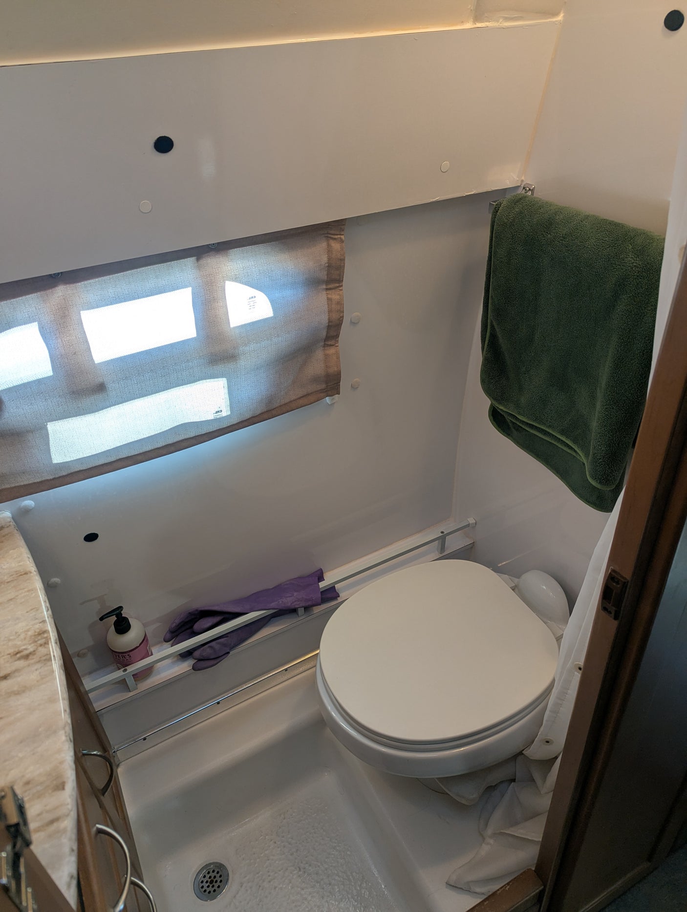 View of a functional RV rental bathroom, featuring a compact toilet, shower base, window with shade, and built-in storage.